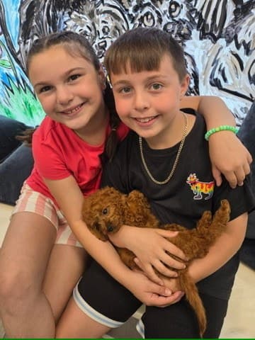 Two siblings welcoming their new red puppy